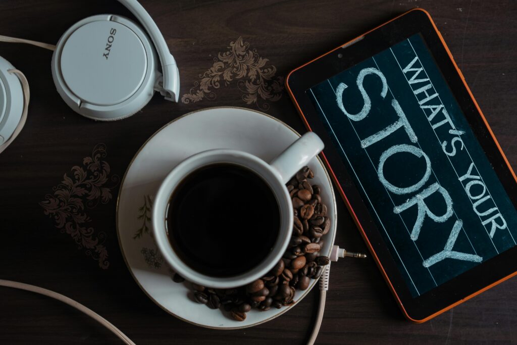 Flat lay of coffee cup, headphones, and tablet with 'What's Your Story' on screen.