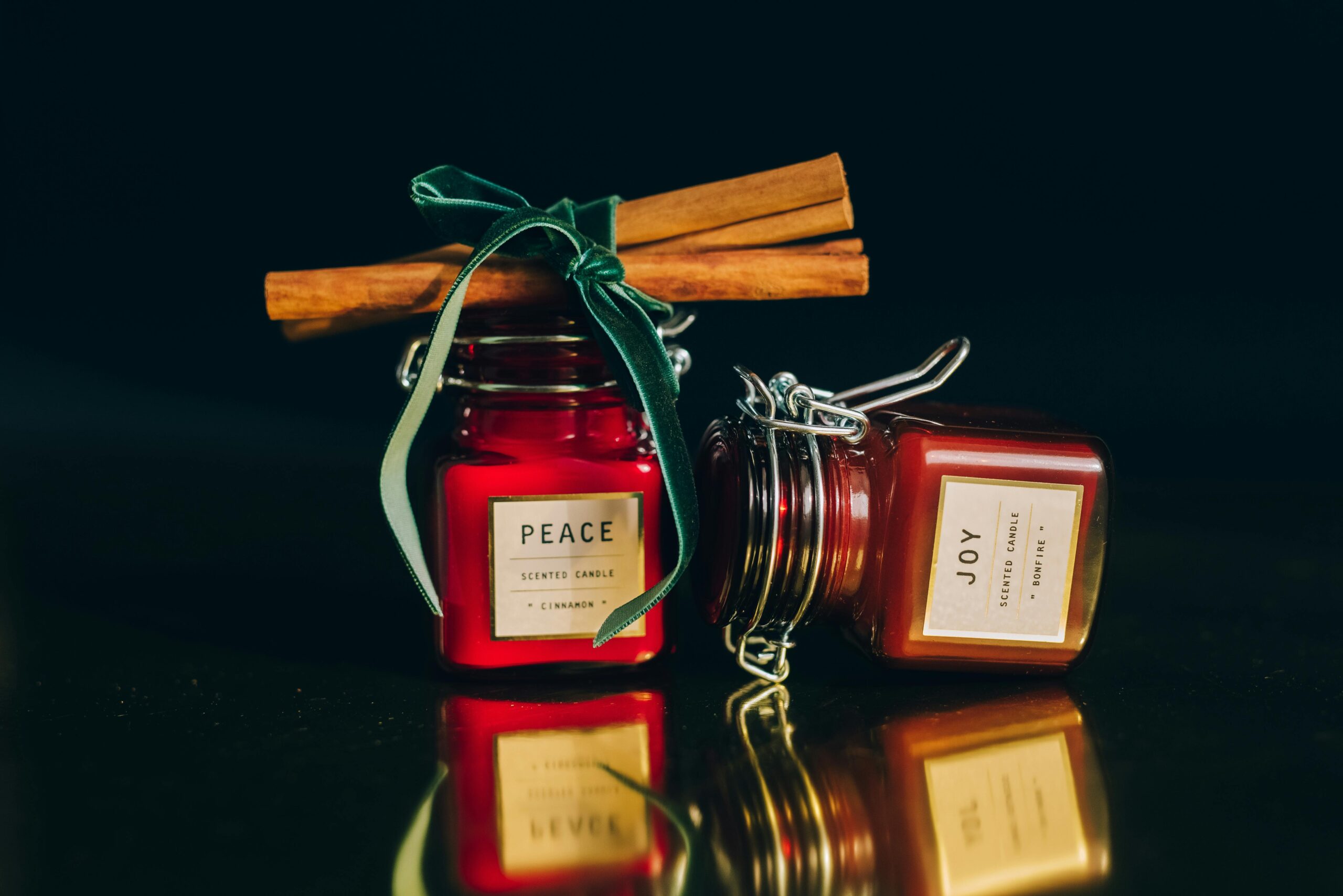 Glass jar scented candles with cinnamon sticks on a reflective surface, perfect for cozy atmospheres.