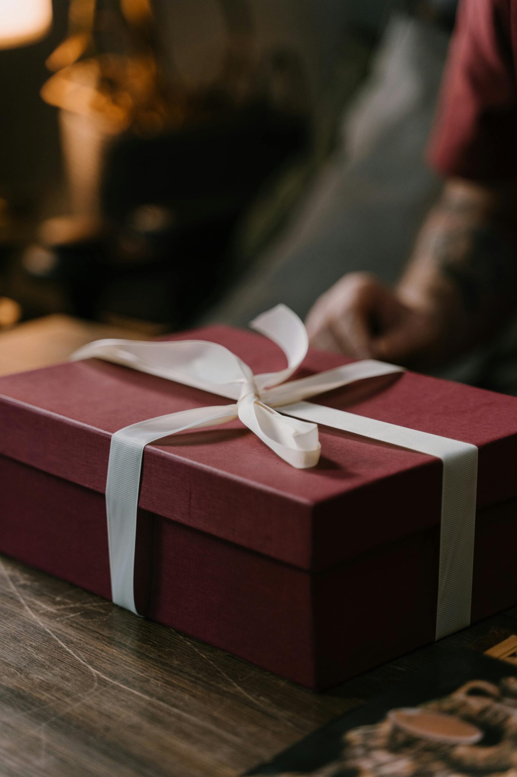 A stylish red gift box with a white ribbon on a wooden surface, perfect for special occasions.